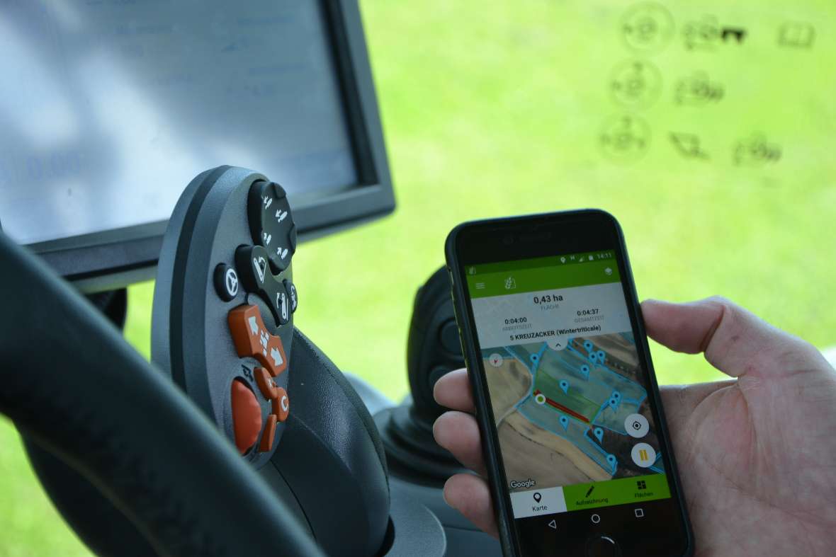 A person sits in the tractor and holds a smartphone in hand (Digital Farming)