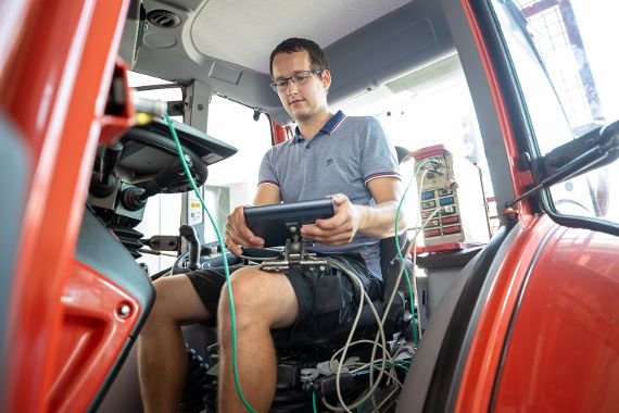 A man in a tractor cabin holds a measuring device in his hand (Agricultural engineering)